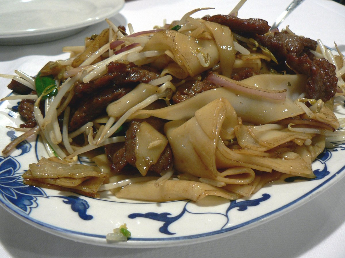 Beef chow fun with wide rice noodles, beef slices, scallions, and bean sprouts.