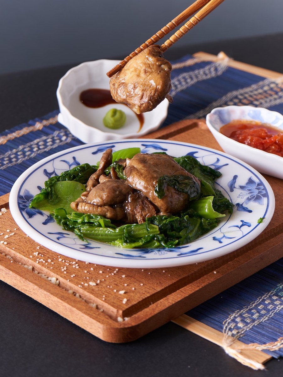 Braised mushrooms with greens on a decorative plate in a glossy savory sauce.