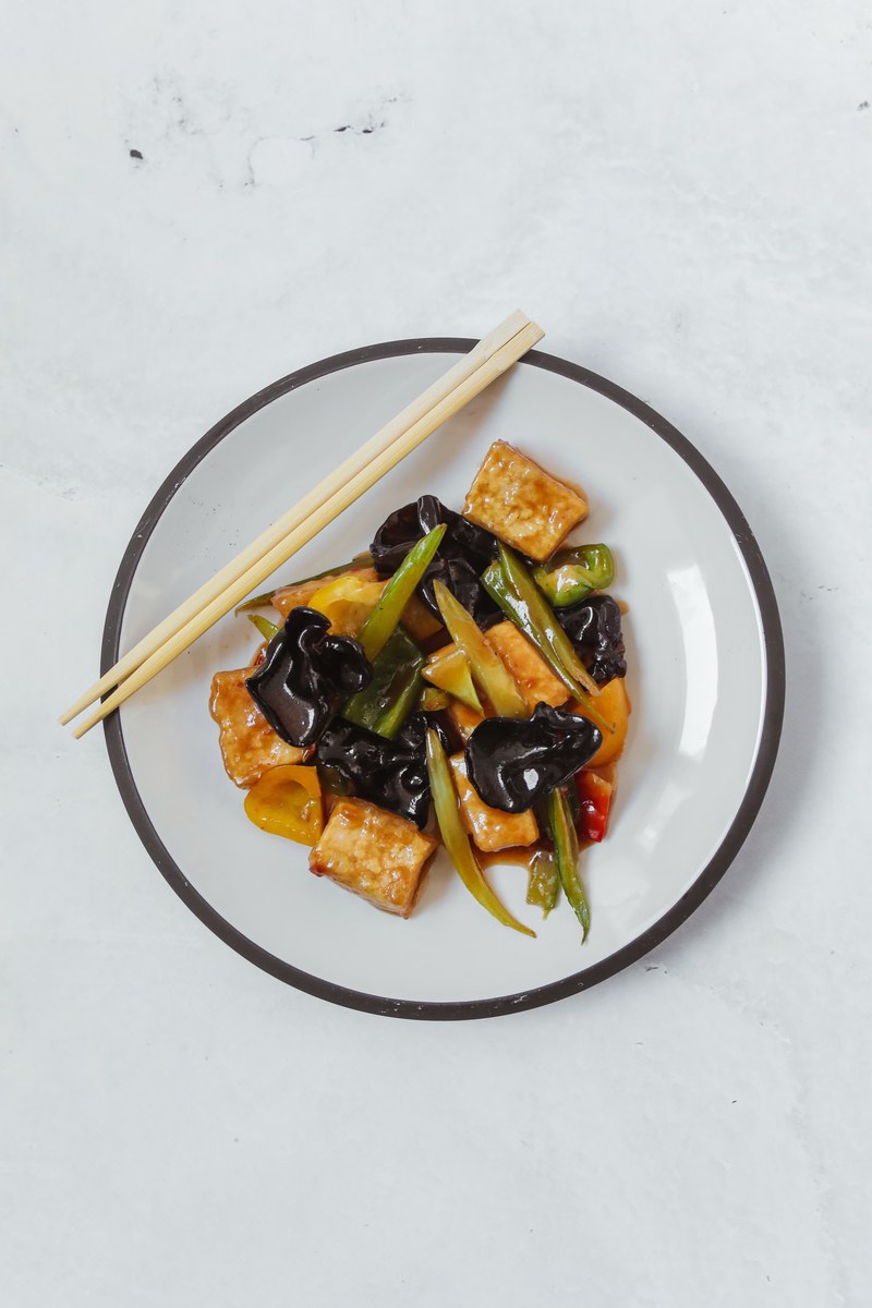 Braised tofu with wood ear mushrooms, peppers, and glossy soy sauce on a plate.