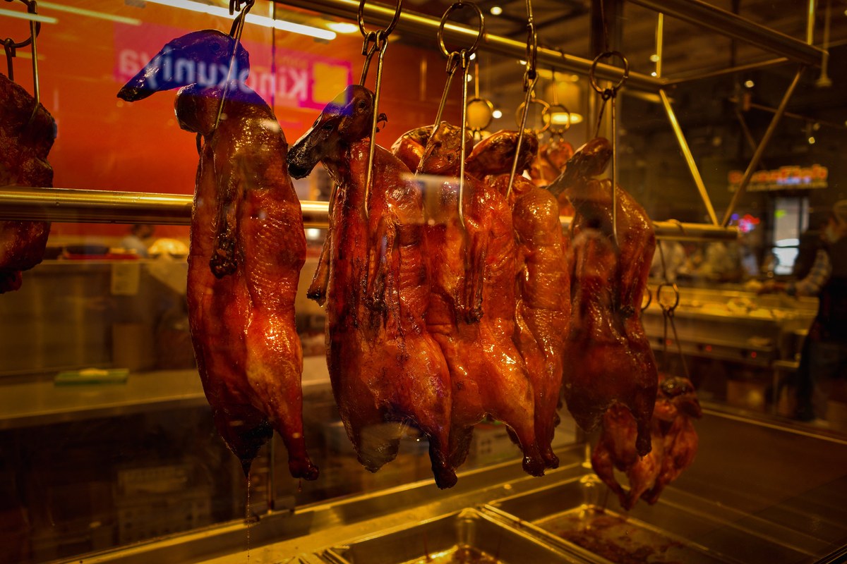 Cantonese roast ducks hanging with glossy lacquered skin in a roast meat shop window.