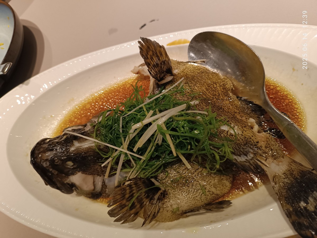 Cantonese ginger-scallion steamed fish with soy sauce and scallion on a restaurant plate.