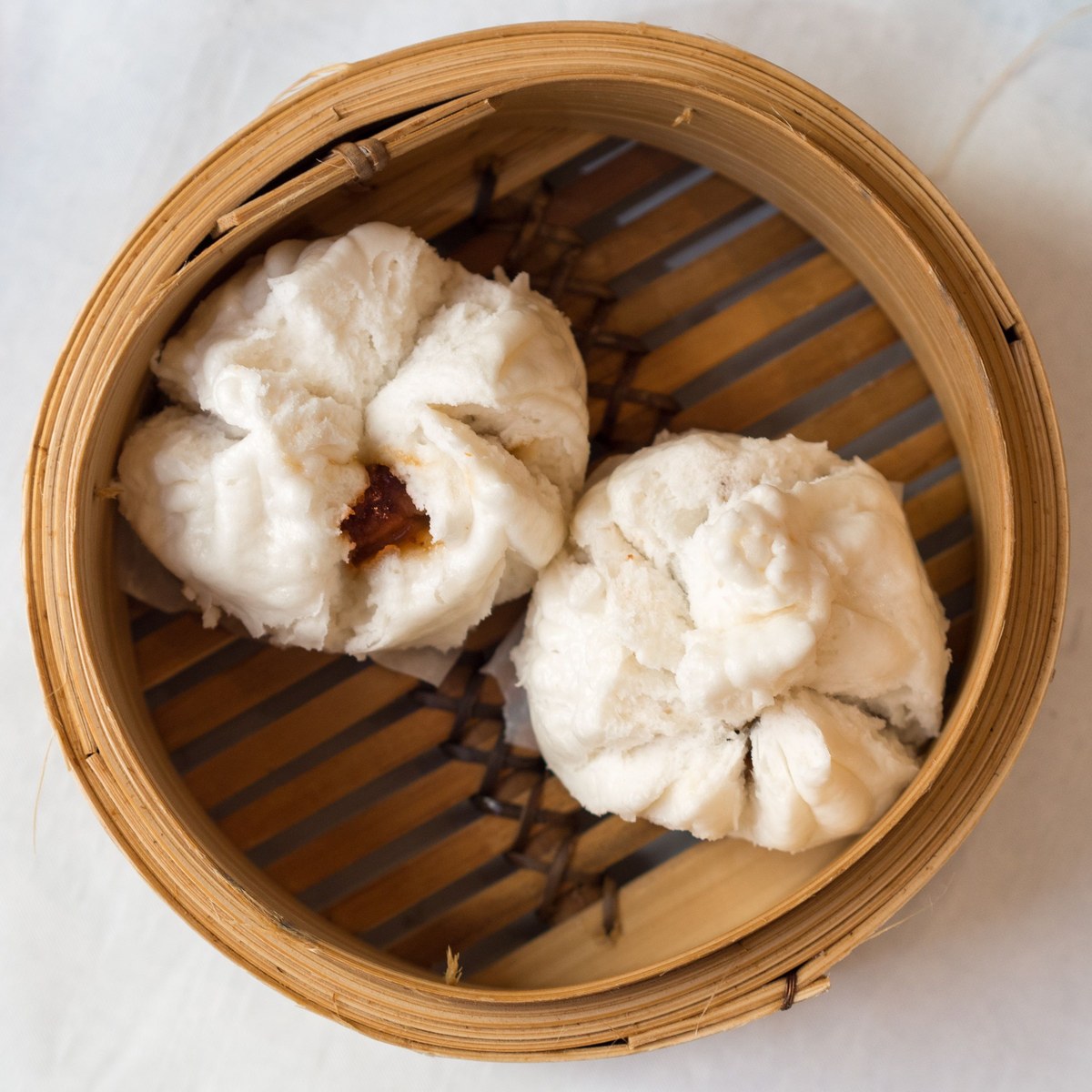 Steamed char siu bao split open in a bamboo steamer with barbecue pork filling
