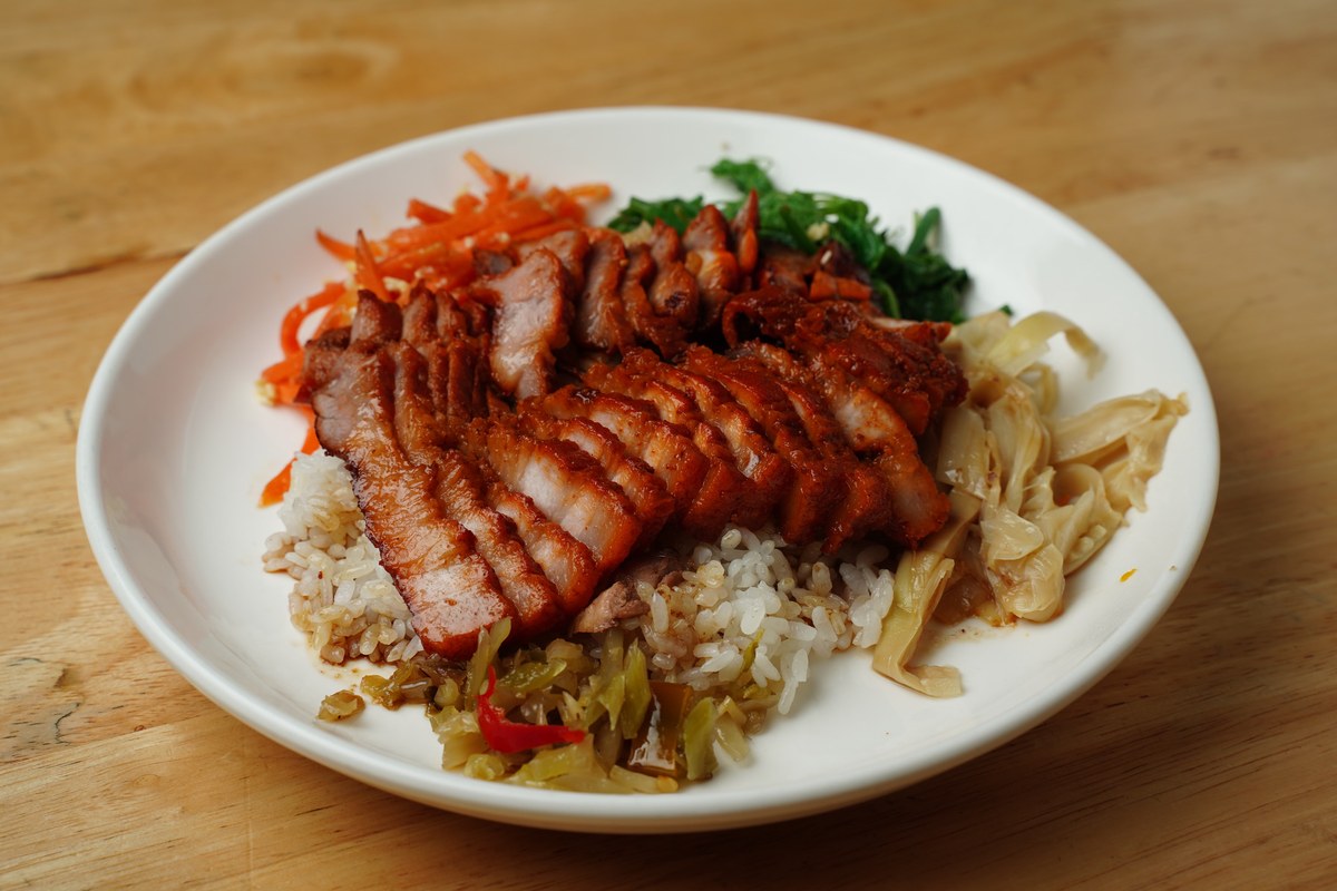 Char siu pork slices served over rice with vegetables in a bowl.