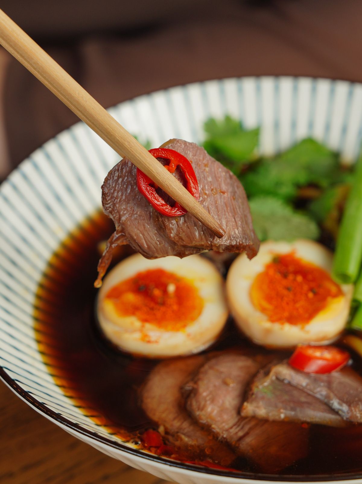 Taiwanese beef noodle soup with sliced beef, soy eggs, cilantro, red chile, and dark broth.