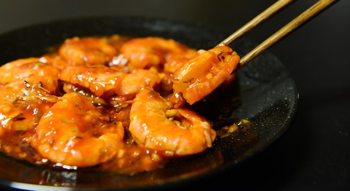 Chili garlic shrimp in a glossy red sauce with chopsticks on a dark plate.