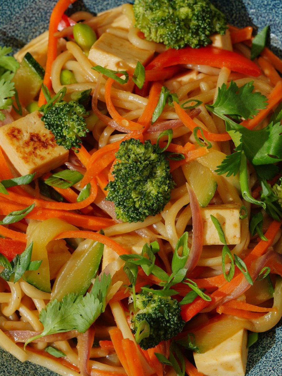 Chili oil noodles with tofu, vegetables, and scallions on a plate.