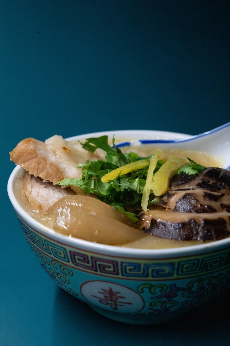 Century egg and pork congee in a patterned bowl with ginger and scallion garnish.