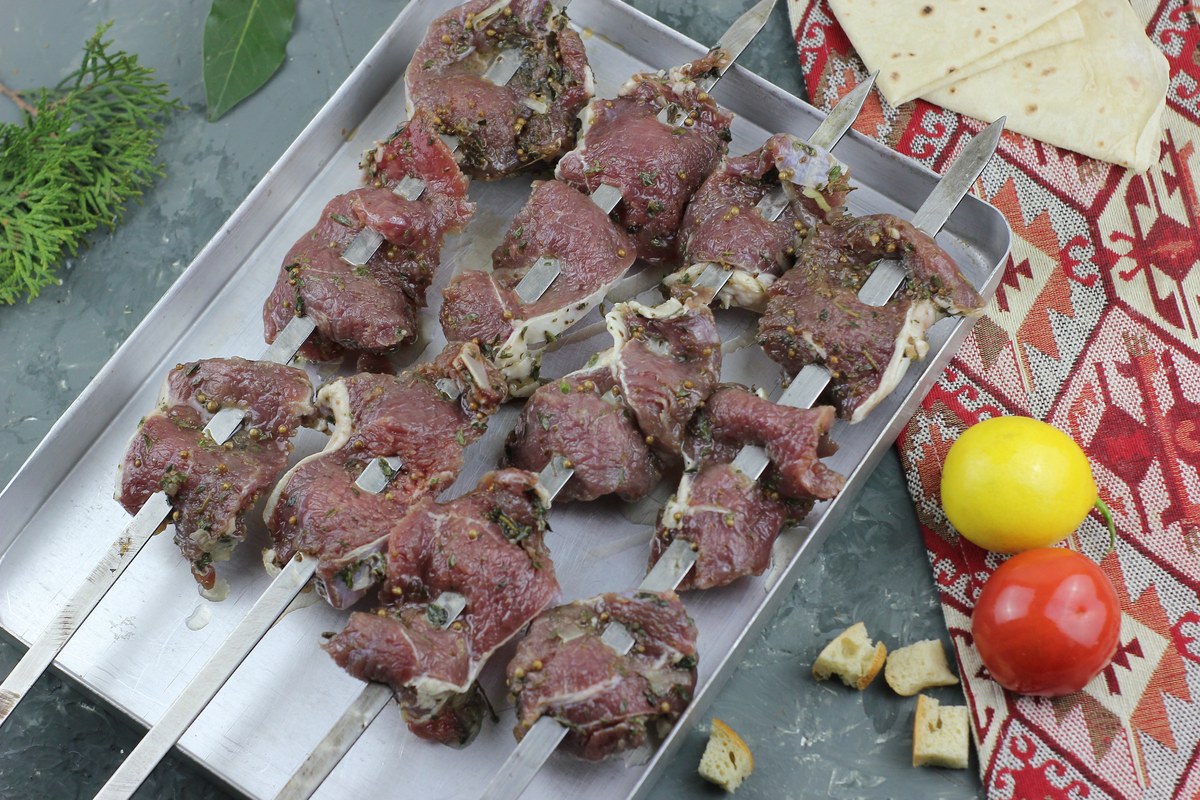 Cumin lamb skewers with browned lamb pieces and vegetables on a tray.