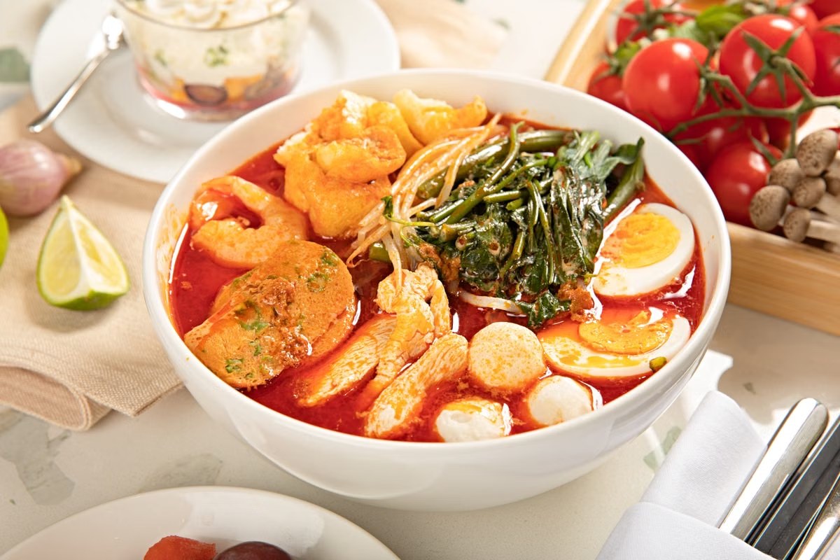 Fish ball seafood noodle soup with red broth, greens, egg, and seafood pieces.