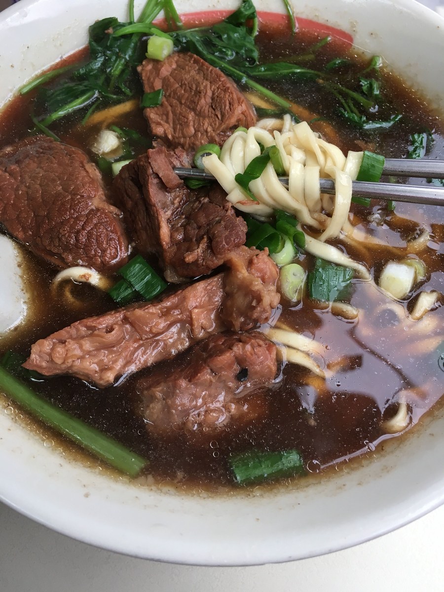 Beef shank noodle soup with sliced beef, dark broth, wheat noodles, and greens.