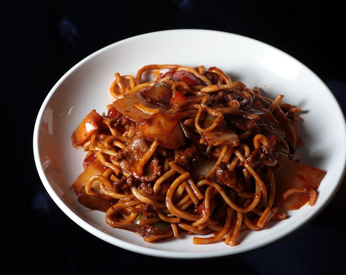 Chinese fried noodles with cabbage pieces, small meat pieces, and glossy brown sauce in a white bowl.