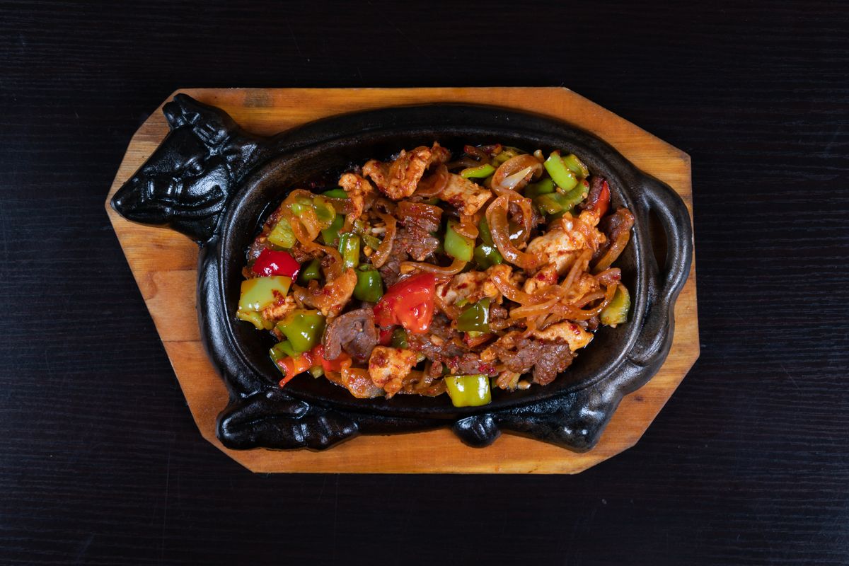 Sizzling beef and pepper stir-fry with onion and glossy black bean sauce on a black hot plate.