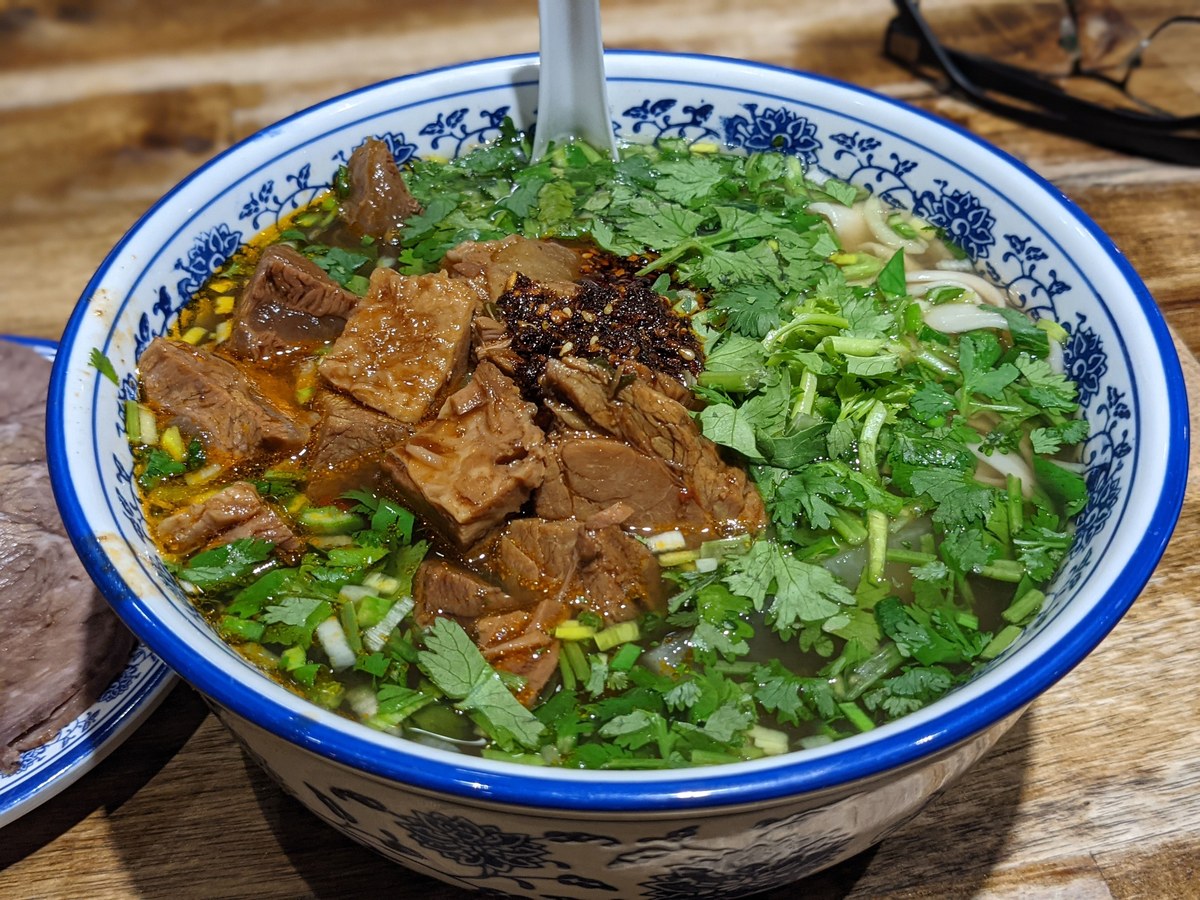 Lanzhou beef noodle soup with beef, herbs, chili oil, and hand-pulled-style noodles.