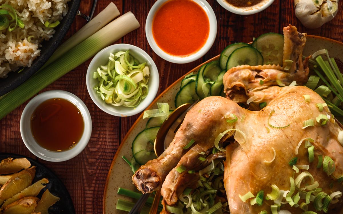 White cut chicken with ginger scallion garnish, cucumber slices, rice, and dipping sauces.