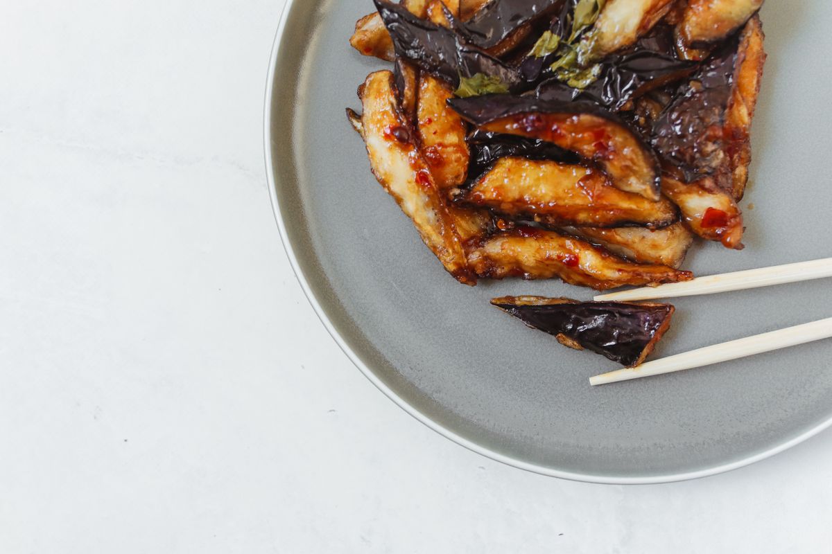 Spicy Chinese eggplant stir-fry with glossy garlic-chili sauce on a gray plate.