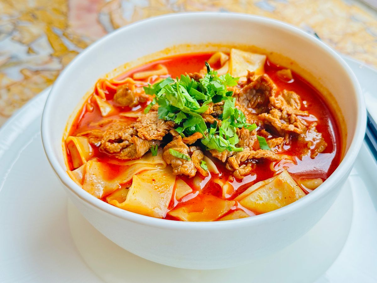 Spicy lamb noodle soup with wide noodles, red broth, sliced lamb, and cilantro.