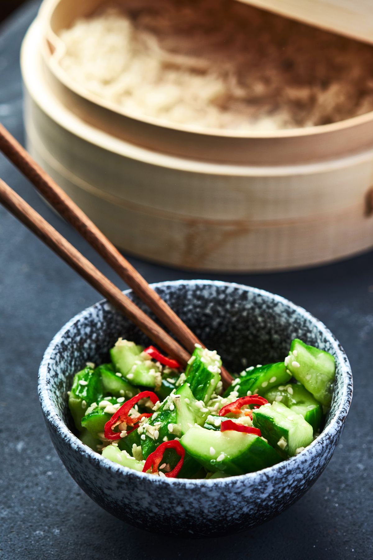Northern garlic cucumber salad with smashed cucumbers, red chile slices, sesame seeds, and chopsticks.