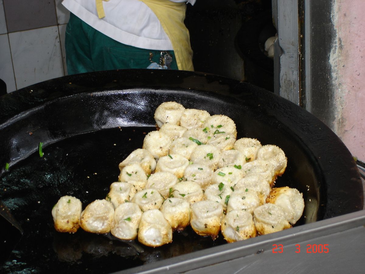 Sheng Jian Bao pan-fried pork buns cooking in a wide griddle with crisp bottoms.