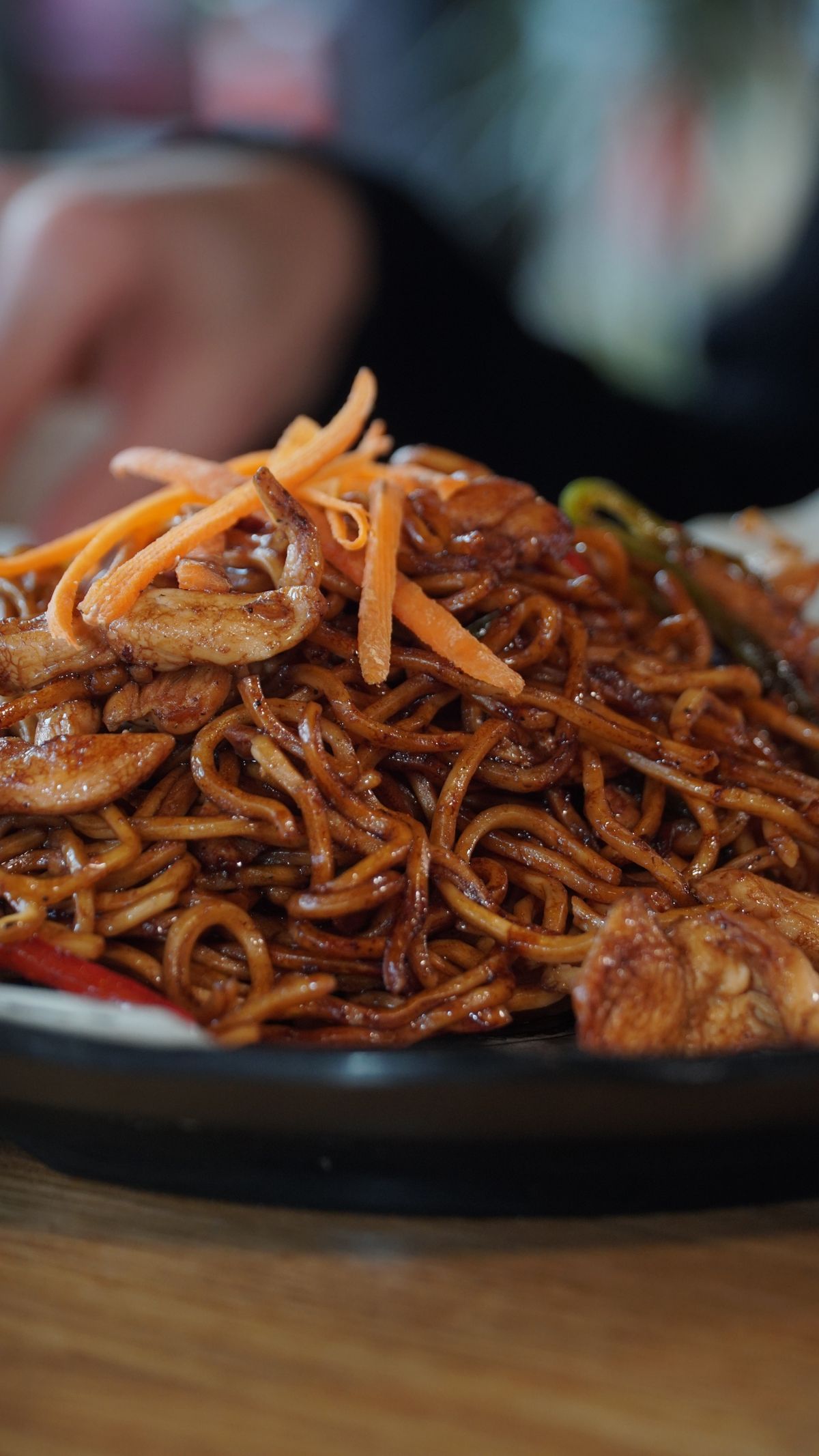 Soy sauce chicken lo mein with glossy brown noodles, sliced chicken, carrot, and greens.