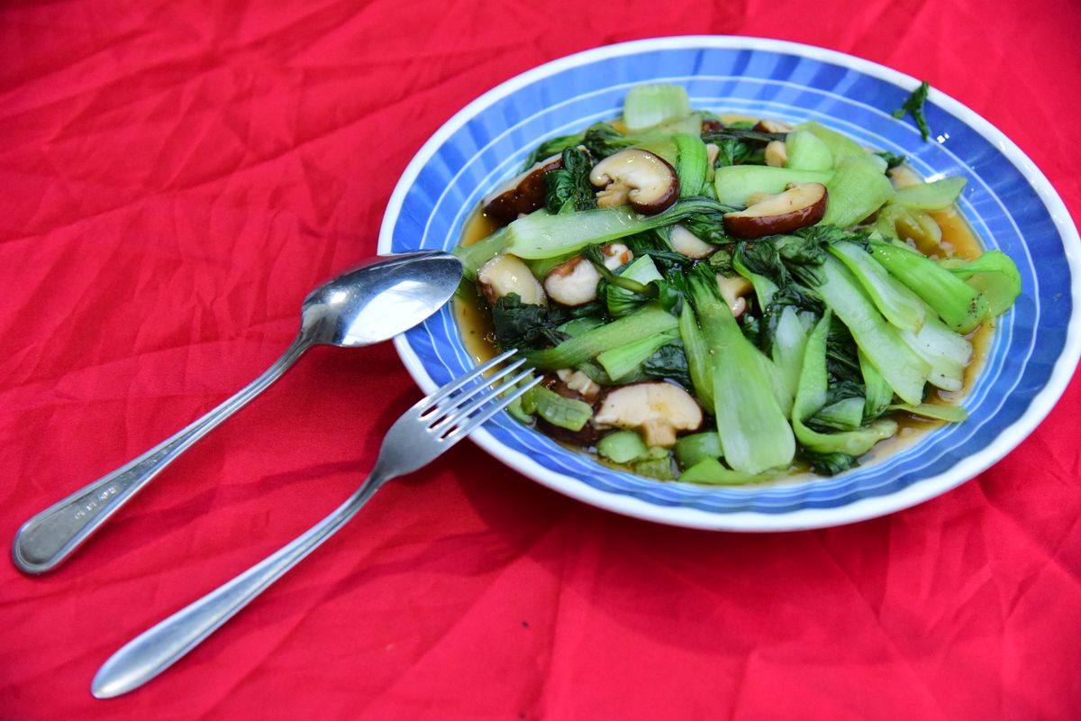 Bok choy and sliced mushrooms in a glossy sauce on a blue plate over a red tablecloth.
