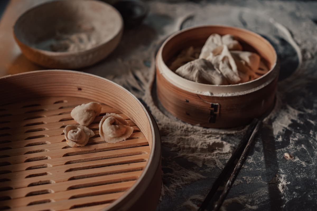 Chinese steamed dumplings arranged in bamboo steamer baskets on a floured work surface.