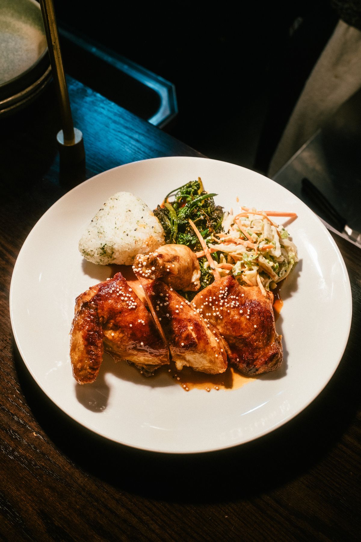 Soy sauce roast chicken pieces served on a plate with rice, greens, and crunchy slaw.