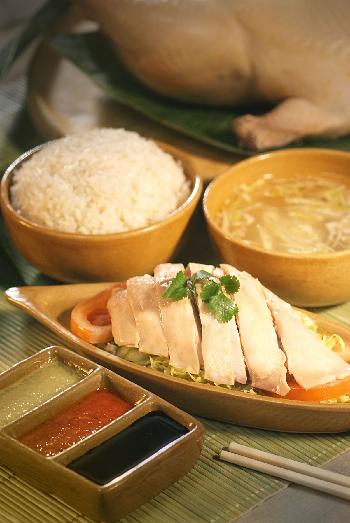 Hainanese chicken rice with sliced poached chicken, rice, soup, cucumber, and dipping sauces.
