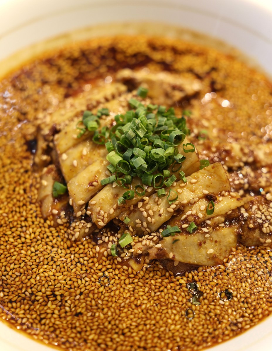 Sichuan saliva chicken slices in red chili oil sauce with sesame seeds and scallions.