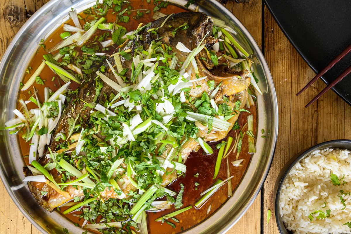 Chinese red-braised whole fish in soy sauce with scallions, cilantro, and rice.