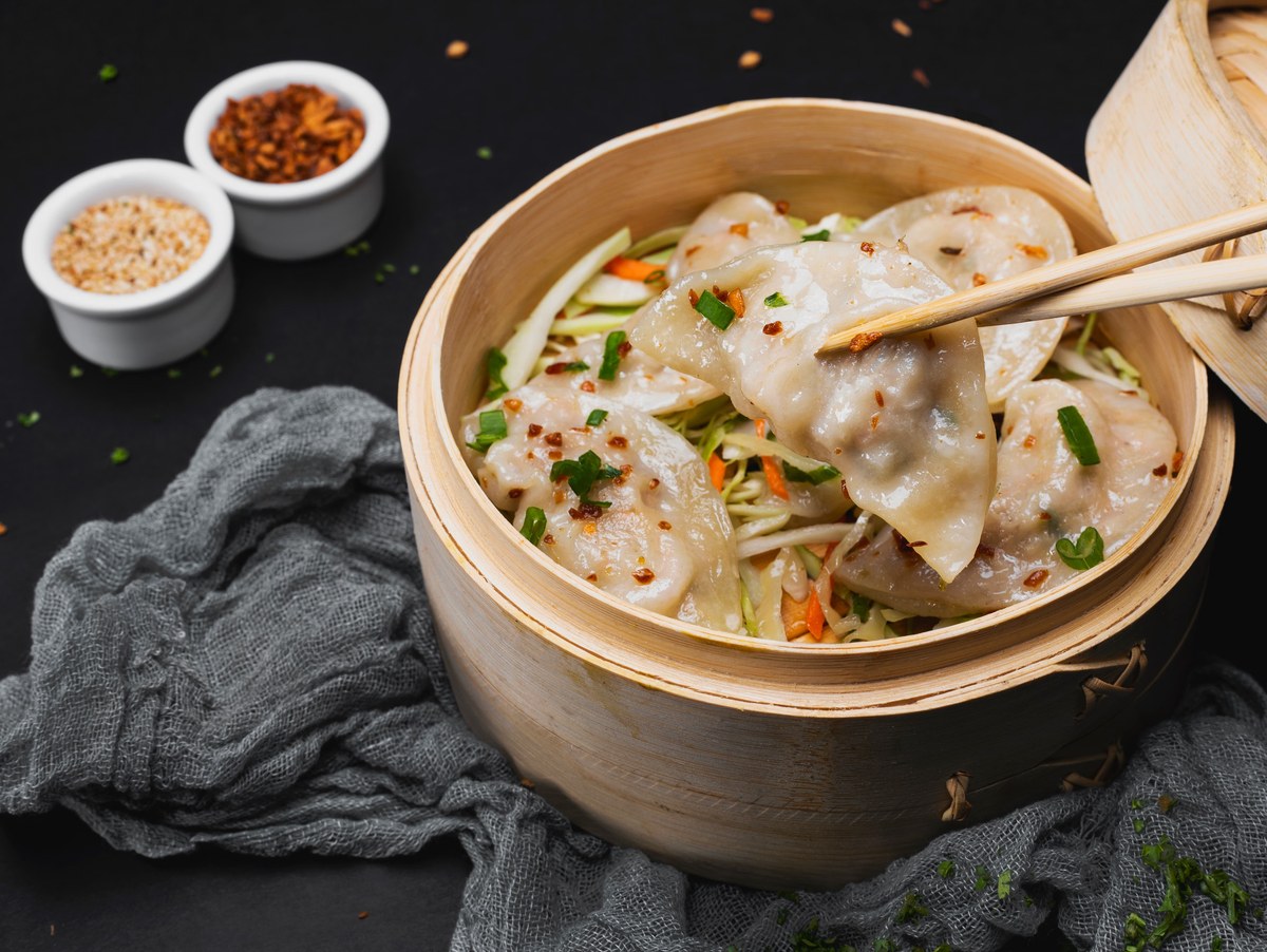 Shrimp and chive dumplings in a bamboo basket with translucent wrappers, herbs, and chili garnish.
