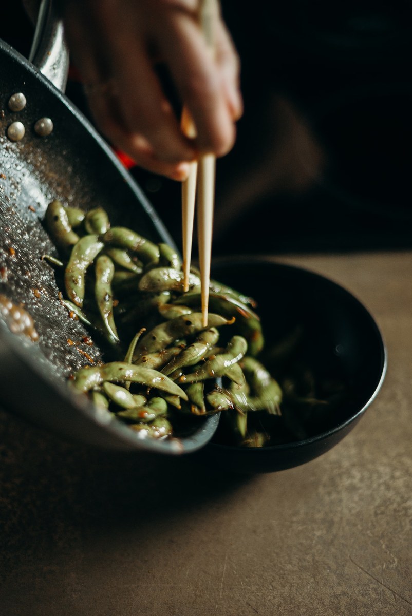 Snow pea stir-fry in a hot pan with crisp green pods and chopsticks lifting the vegetables.