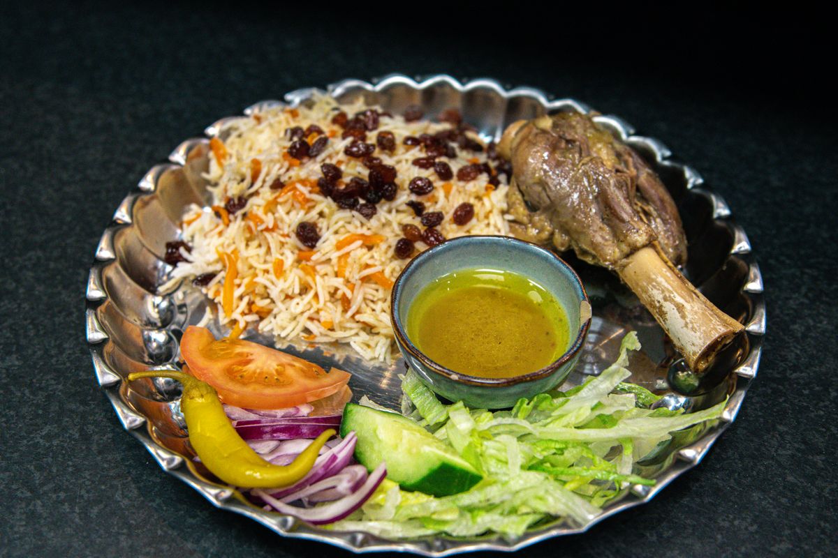 Xinjiang-style lamb pilaf with rice, raisins, carrot, lamb shank, cucumber, onion, tomato, and yellow pepper.