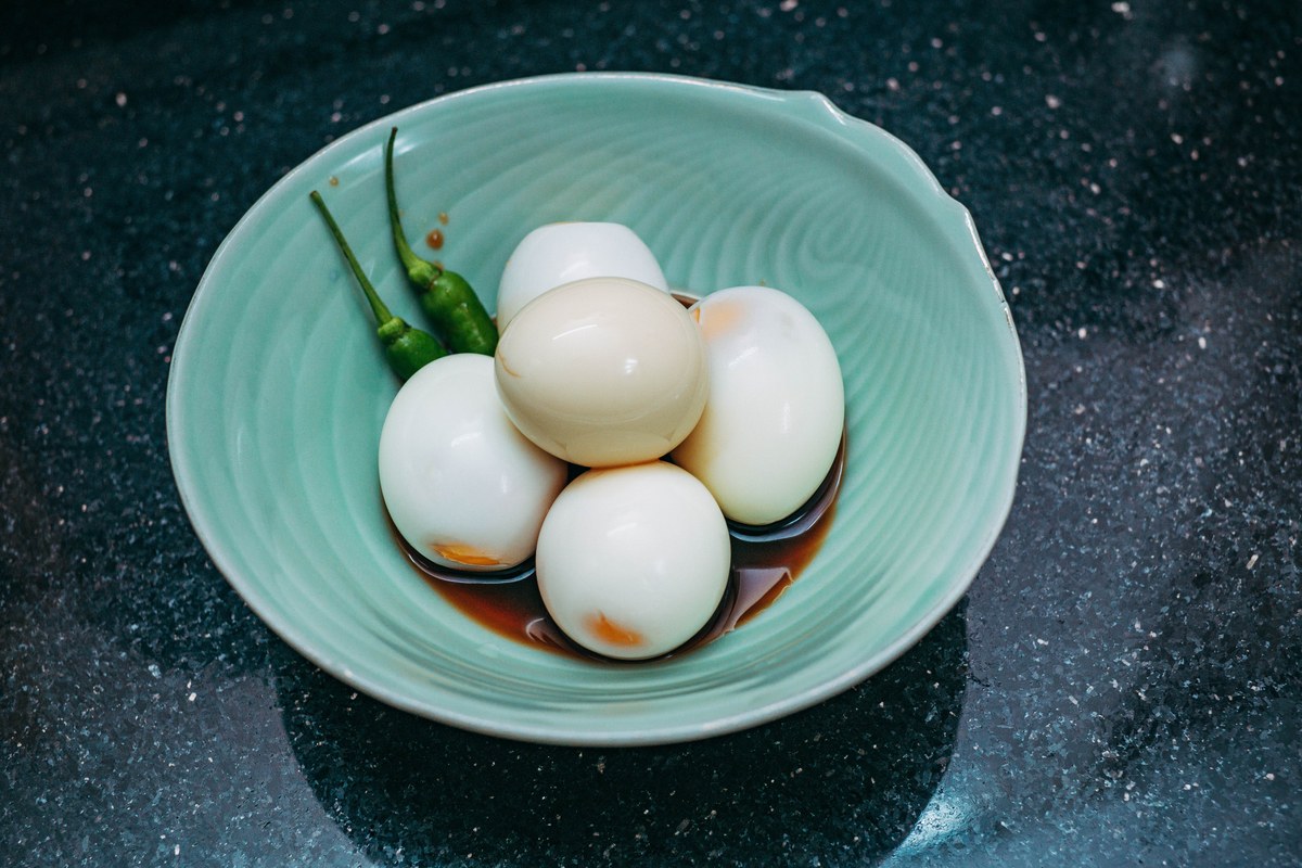 Soy sauce eggs in a bowl with soy marinade and green chilies.