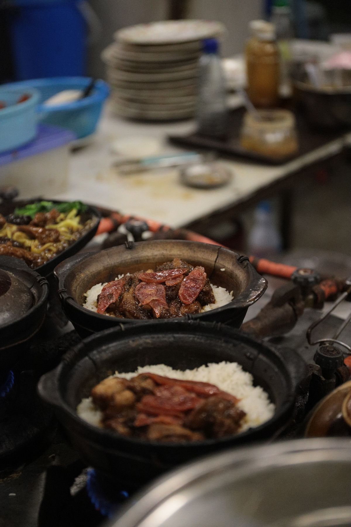Clay pot rice with Chinese sausage and savory meat cooking over a stove.