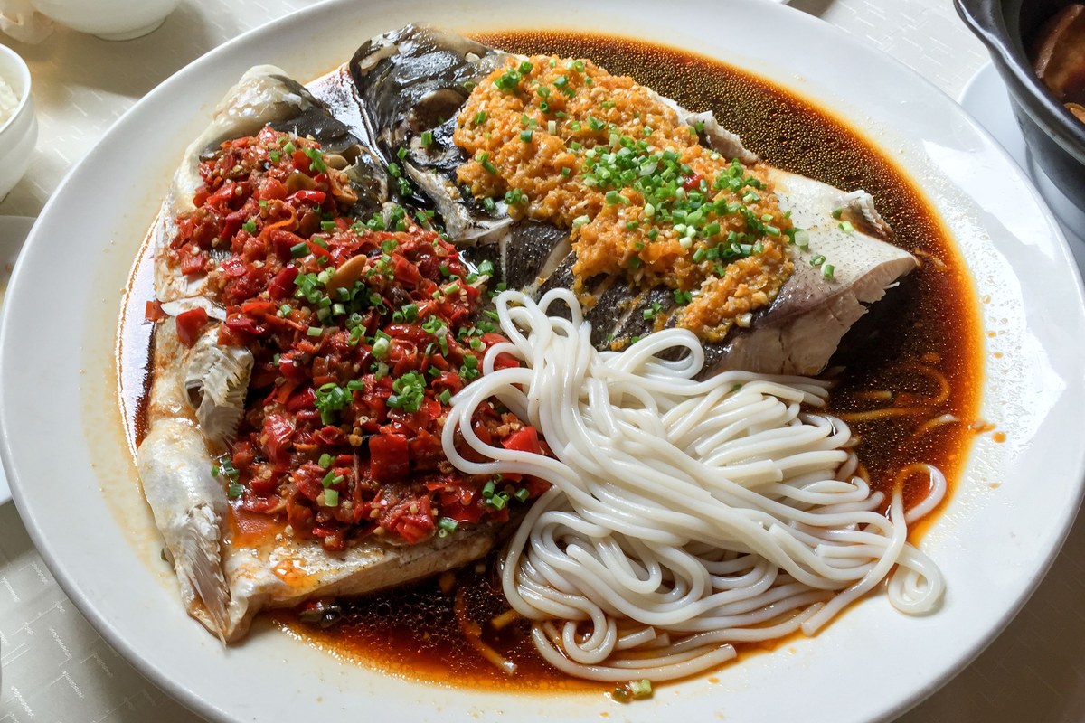 Hunan steamed fish head covered with chopped red chili peppers on a large serving plate.