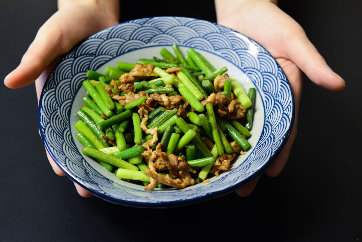 Pork and garlic scape stir-fry with bright green scape segments and thin pork pieces in a blue bowl.