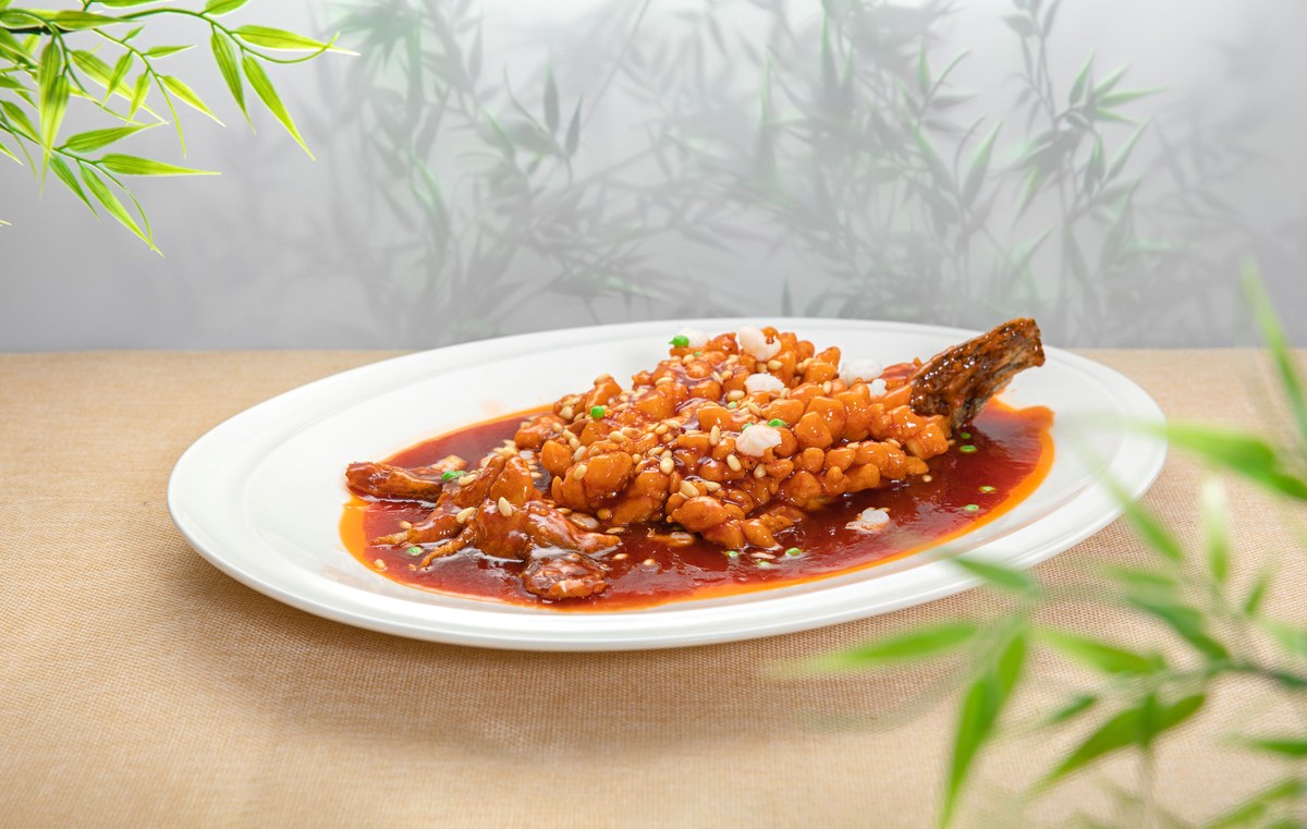 Crisp whole sweet and sour fish in glossy red sauce on a white plate.