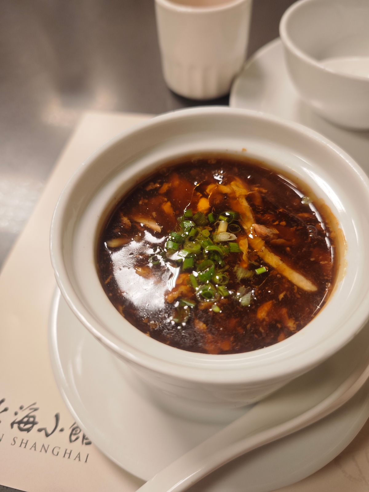 Hot and sour egg drop tofu soup with dark broth, scallions, mushrooms, and egg ribbons.