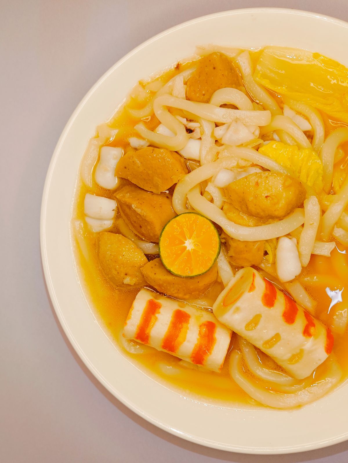 Chinese fish ball noodle soup with fish cake, cabbage, thick noodles, and light orange broth.