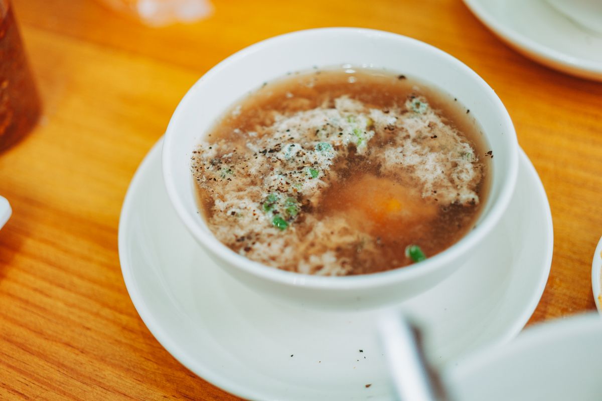 Tomato tofu soup with soft tofu pieces, pale egg ribbons, scallions, and orange-red broth in a white bowl.