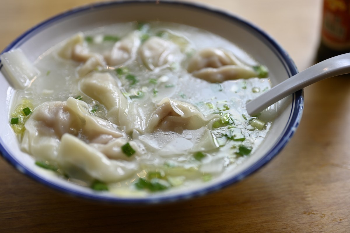 Wonton soup in clear broth with folded wontons in a ceramic bowl.
