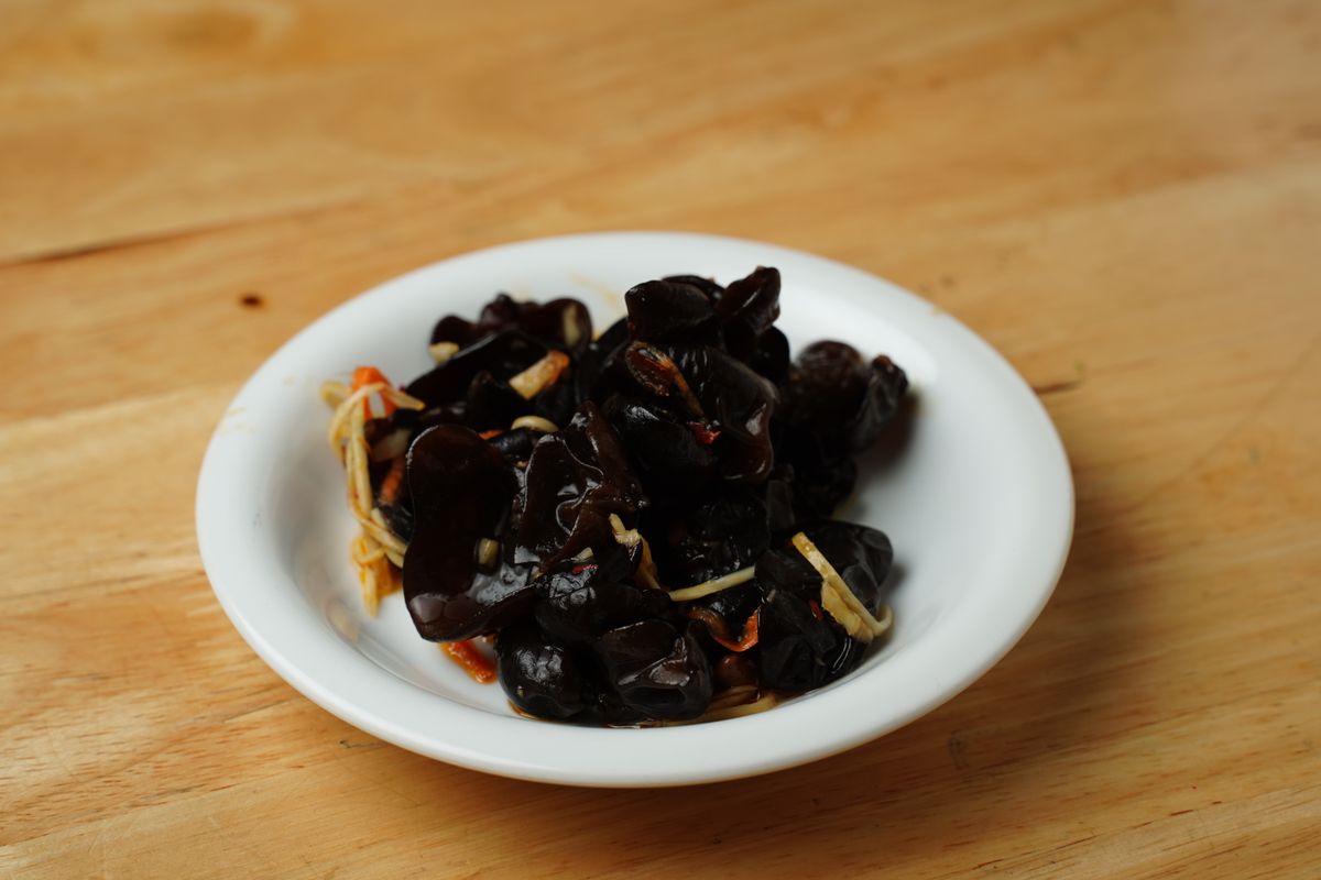 Chinese wood ear mushroom salad in a white bowl with garlic, chili dressing, and glossy black mushrooms.